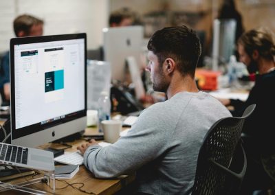 man in gray sweatshirt sitting on chair in front of iMac